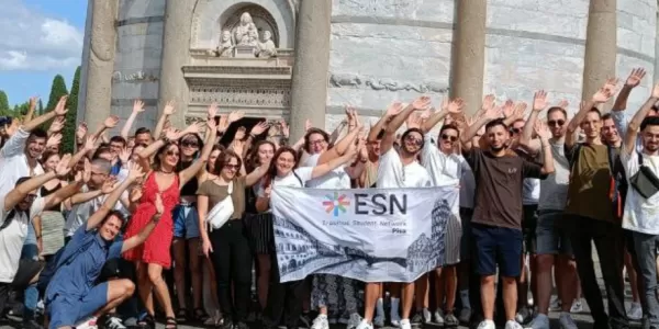 Group of people with Pisa Tower on the back and a flag of ESN Pisa.