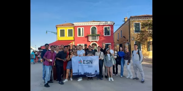 Group picture of the students and the volunteers holding the ESN Venezia flag in front of some colorful houses in Burano