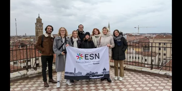 The international students and the volunteers are standing in a group on the terrace of the conservatory of Venice in while holding the flag of the association