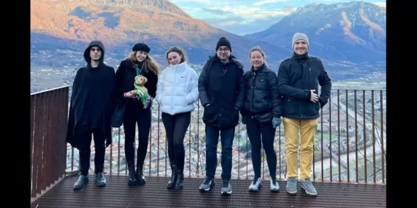 Group of students standing on a terrace with the landscape of Trento's mountains in the back