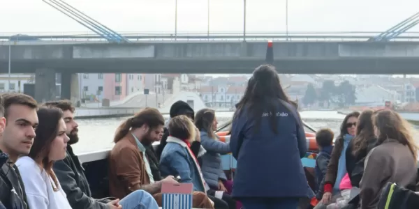 A group of international students are sitting on a moliceiro crossing a bridge.