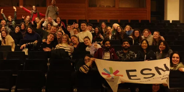 A large group of ESNers and Erasmus are sitting down and smiling with the ESN flag besides them.