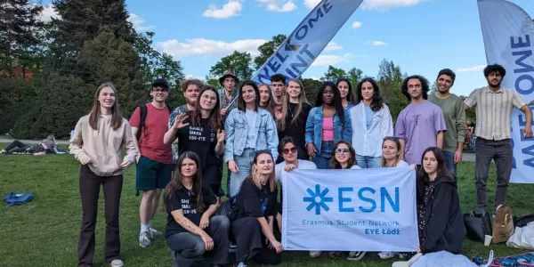 The image shows participants of the event holding the ESN-EYE flag in a park in Lodz during the picnic after the team competition.