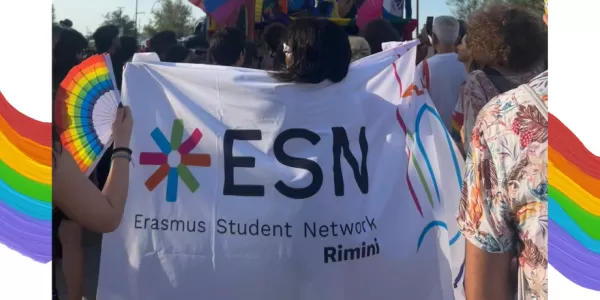 Woman walking in the middle of the parade with the ESN Rimini flag on her shoulders; on the side of the photo there are some graphic elements related to the Pride theme.