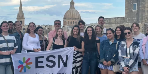 Students standing in front of a scenic view of Valletta, holding the ESN flag