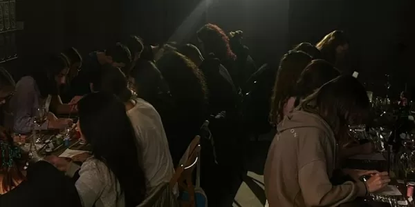 A group of young people sitting at tables in a dimly lit room, focused on painting during a Sip & Paint event.