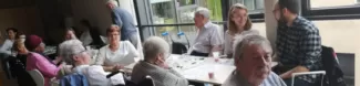 Several elderly people and young people sitting together next to a table.