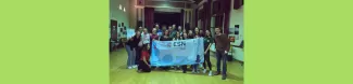 A group of international students and volunteers is standing in a room holding the ESN Trieste flag and smiling.