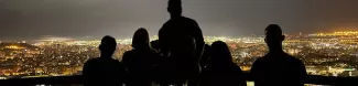 Silhouettes of the five participants with the bright Barcelona skyline behind them. The sky is dark and the photo is only illuminated by the lights of the city.