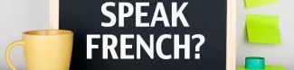 This image represent a black board were the words "Speak French" are written. On the left there is a cup of coffee, and on the right some post-it notes are glued on the wall.