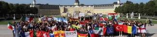 Group Picture of all participants with group & country flags in front of the castle in Karlsruhe