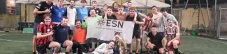 Group of international students with ESN Modena flag on a futsal pitch