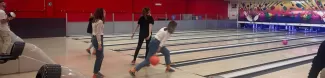 In the photo, a girl is captured in the midst of her bowling action, her focus intense as she swings her arm forward to release the ball. Her posture is dynamic, embodying both concentration and grace.