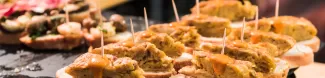 Foto of small portions of food, several pieces of spanish tortilla on top of bread slices are on the front of the picture