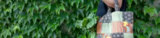 A person holding a colorful tote bag on their shoulder, a green bush is the background.