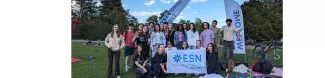 The image shows participants of the event holding the ESN-EYE flag in a park in Lodz during the picnic after the team competition.