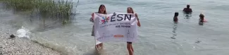 Two international students holding the ESN ASE Verona flag while standing in the lake