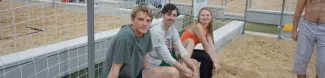 Three people smiling on a beach volleyball arena